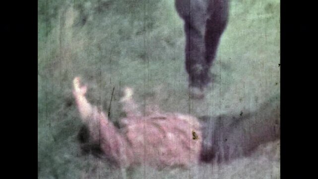 Man murderer wiping bloody knife after killing enemy. Murder scene reconstruction. Male killer standing over dead man outdoor. Crime thriller. Suspense-themed archive. Vintage color film. Retro 1960s