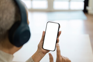 A man is holding a cell phone with a white screen and blue headphones on
