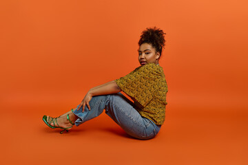 Stylish African American woman seated, legs crossed, vibrant background.