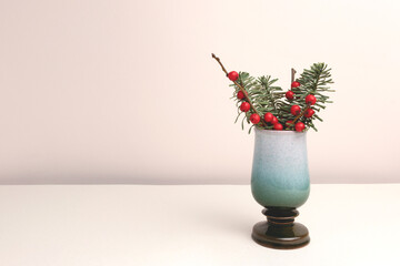 Fototapeta premium Nobilis fir and winterberry branches in a vase in front of beige background. Place for text.