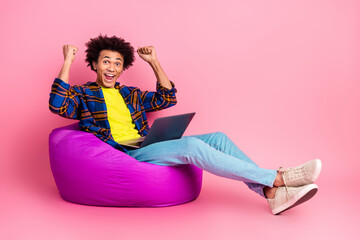 Photo of cheerful positive young man wear clothes use netbook sit soft pouf success isolated on pink color background