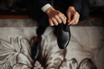 A man is putting on his shoes. The shoes are black and the man is wearing a suit