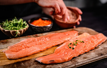 Fresh trout salmon filet with herbs greens on wooden board and chief hands on blurred background. Omega orange fish with rosemary for healthy nutrition