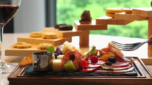 Elegant charcuterie board with assorted fruits, cheese, and cured meats in fine dining restaurant, accompanied by glass of red wine and gourmet desserts in background. Fine Dining and Culinary Art.