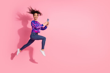 Full length photo of cheerful pretty lady dressed retro sweatshirt jumping high texting modern device empty space isolated pink color background