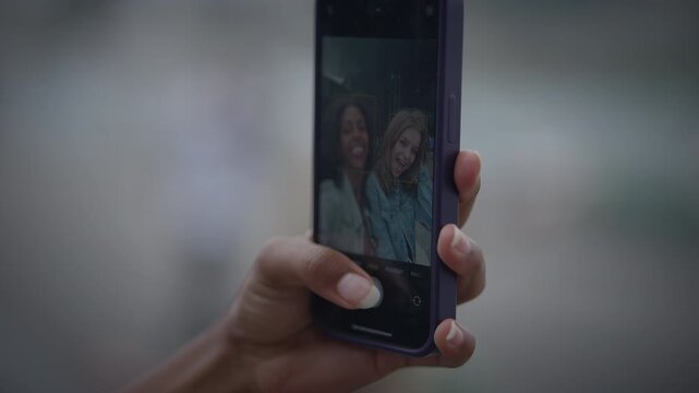 Closeup photo of a hand holding a smartphone to take a selfie with blurred background