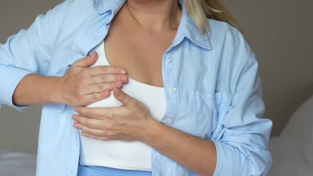 The girl suffering from a pain in her breast during menstruation. Cropped shot of young blonde woman checking breast feeling discomfort on a grey background. Self-examination 