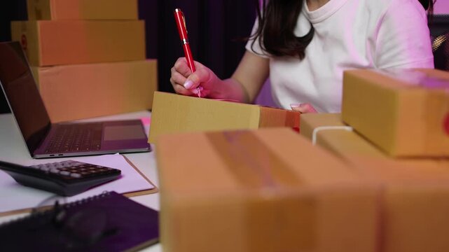 A woman who works as an online seller from home writes recipient addresses to prepare for delivery of an internet order.