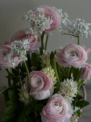 Beautiful tender pink ranunculus flowers, white ornithogalum and hyacinths flowers in a floral composition, close up vertical view on the grey wall background 