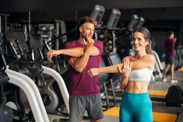 Fototapeta premium A fit young adult couple doing stretching exercises together at the gym