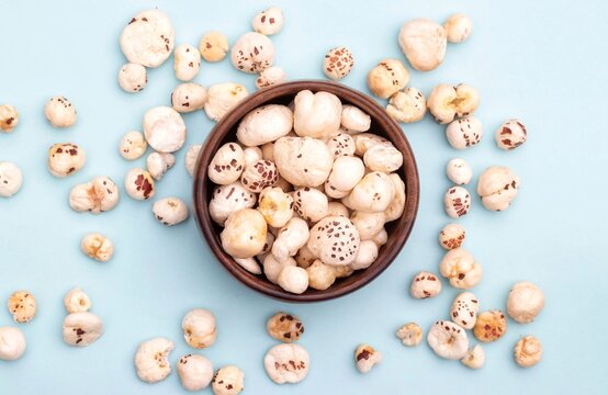 Top View of Makhana or Fox Nut in a Wooden Bowl Isolated on Light Blue Background with Copy Space, Also Known as Lotus Seed Pop, Euryale Ferox or Gorgon Nut