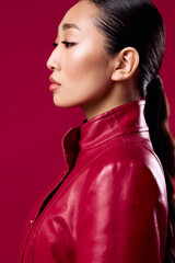 Fashionable asian woman in red leather jacket, with hair in ponytail, looking off to the side