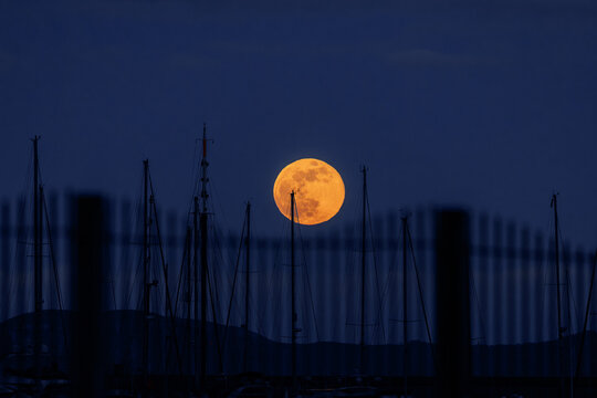 24 FEBRUARY 2024 wolf moon rising over the harbour at Weymouth, Dorset, UK, blue sky, pink moon, boat masts and fence