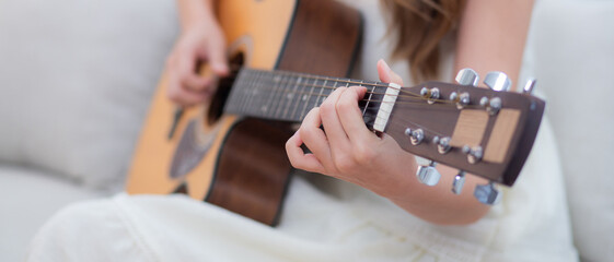 Closeup hands of young asian woman sitting on sofa playing guitar in living room at home, skill and practice, guitarist and hobby with enjoyment and relax, entertainment and lifestyle.