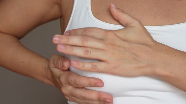 Close up of a young woman feeling discomfort in her breast suffering from a pain during menstruation. Cropped shot of a girl checking breast groping for seals on a grey background. Self-examination