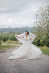 A bride is posing for a picture on a road with a veil over her head. Scene is joyful and celebratory, as the bride is dressed in a beautiful wedding gown and is smiling for the camera