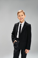 Stylish preadolescent boy in a suit and tie against gray backdrop.