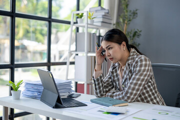 A woman is sitting at a desk with a laptop and a stack of papers