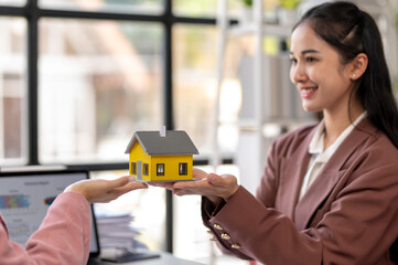 A woman in a suit holding a yellow house model