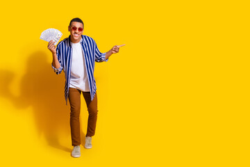 Fototapeta premium Full size photo of successful man dressed striped shirt in sunglass hold money directing empty space isolated on vivid color background