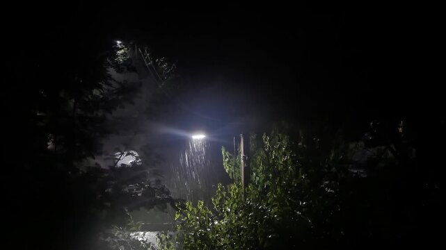 night rain with a thunderstorm. one street lamp shines during rain and lightning. drops of night rain fly by in the light of the lamp. night cityscape with summer rain. night rain view from the window