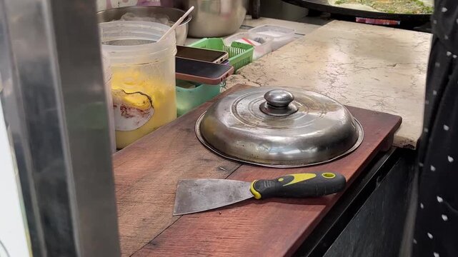 A person makes Indonesian dessert Terang Bulan, pouring batter onto a griddle and adding toppings. The process shows the dessert's golden crust and delicious fillings