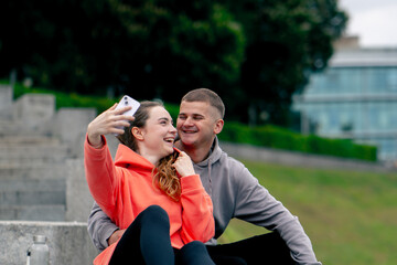 In the park a young couple in love after sports relaxing hugging on a concrete parapet taking...