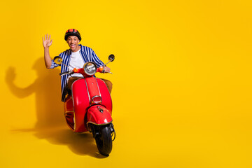 Full size photo of nice optimistic man dressed striped shirt in helmet driving motorcycle waving palm isolated on vivid color background