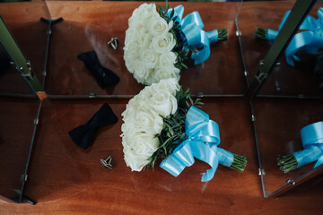 Two bouquets of white roses and blue ribbons are displayed on a wooden table. The arrangement of...