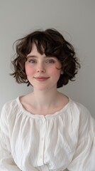 A young woman with long black hair is standing in front of a gray background. She is wearing a shirt and has a gentle smile on her face