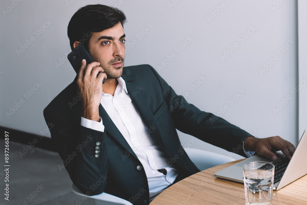 Aufkleber serious indian employer making cellular call sitting at desktop with netbook and thoughtful looking 