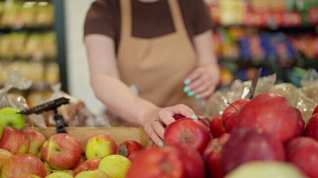 Close-up of a girl supermarket worker in a brown T-shirt and apron arranging apples on the counter during her work shift at the supermarket