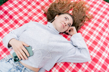 in the park on a red checkered blanket a girl with blue eyes lies on her back hands behind her head...