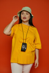 An Asian woman posing in a studio, wearing a yellow shirt and a green hat.