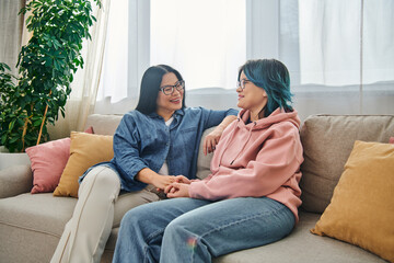 An Asian mother and her teenage daughter in casual wear having a heartfelt conversation while sitting on a cozy couch.