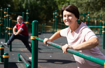 Mature woman doing push-ups from the crossbar on outdoor sports ground