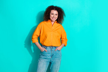 Photo of positive cheerful woman with wavy hair dressed orange shirt jeans holding hands in pockets...