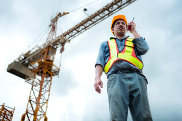 Portrait of crane worker uses walkie-talkie communicate with tower crane operators to lift and move objects on building construction sites