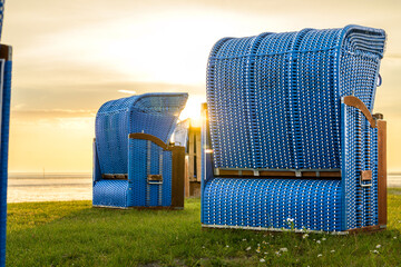 Obraz premium Beach Chairs in sunset on grassy coast line at North Sea Germany