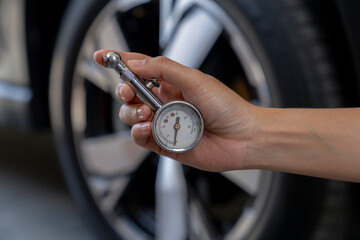 Obraz premium A young woman is checking her car's tire pressure before a trip.