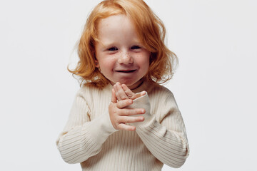 Redhaired little girl in white sweater with hands covering face, captured in a moment of timid beauty