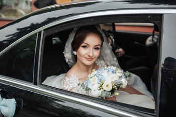 A bride is sitting in a car with a bouquet of flowers. She is smiling and looking out the window