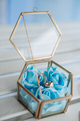 A gold and blue box with a blue rose and two gold rings inside. The box is placed on a table
