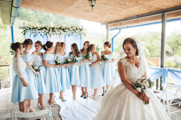A bride is standing in front of a group of bridesmaids, all wearing blue dresses. The bride is...