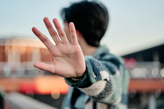 young asian man covering his face in a stop sign. young celebrity covering his face with the palm of his hand and looking away to avoid paparazzi.