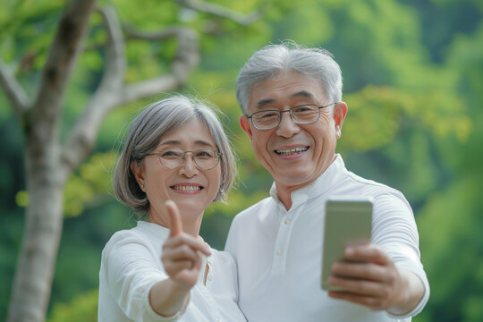 スマートフォンを使って自撮りするシニアカップル。初夏の新緑。