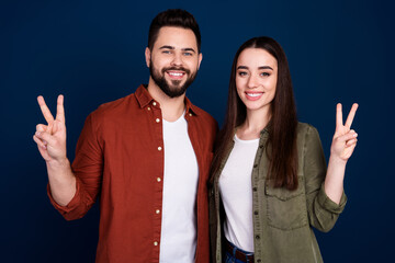 Photo of cheerful lovely pretty couple wife husband wear stylish clothes v-sign isolated on dark blue color background