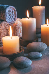 Spa still life with burning candles, towels and stones on grey background.