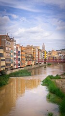 Fototapeta premium Colorful buildings along the Onyar River in Girona, Spain under a partly cloudy sky.