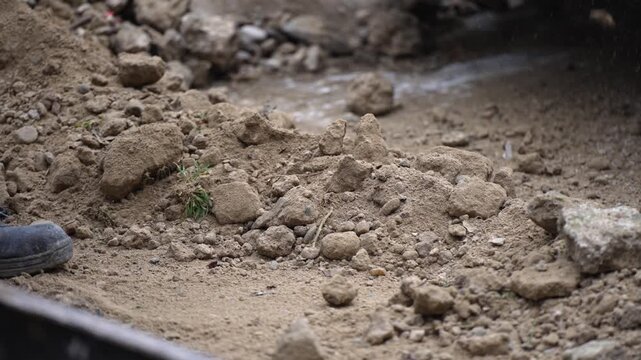 Manual laborer shoveling soil at a construction site. A close-up image of a construction worker's boot and a shovel digging through rocky soil